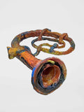 Ceramic work resembling an instrument such as a french horn or tuba with a unique design on a white background.