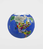 A handmade globe sculpture shown against a white background, with bright blue oceans and collaged paper landmasses. North and South America are visible, filled with colorful patches of green, yellow, red, pink, and gray.