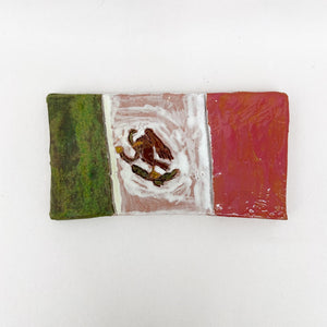 This ceramic piece represents the Mexican flag, featuring the traditional green, white, and red tricolor, with the national emblem of an eagle perched on a cactus in the center. The hand-painted glaze exhibits a textured finish, imparting a rustic quality that emphasizes the handcrafted nature of the object while celebrating national symbolism.
