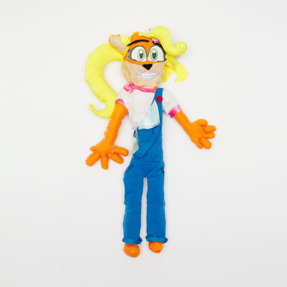 ‘A Coco Bandicoot Plushie’ is a satin, flannel, jersey and cotton fabrics, polyfil and paper doll that measures 26 by 19 by 4in. Coco Bandicoot is the little sister of Crash Bandicoot, a video game originally created in 1996. The subject, Coco, is a humanoid version of an Australian bandicoot, who wears a white t-shirt and blue overalls. She has blonde hair and orange fur. Coco is described as the highly intelligent and spirited secondary protagonist in the Crash Bandicoot games. 