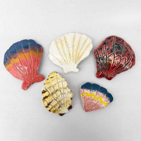 This collection of ceramic seashells showcases a variety of colors and patterns, with each shell individually glazed in hues ranging from naturalistic whites and tans to vibrant reds, blues, and yellows. The delicate grooves and ridges on each piece enhance their textural detail, reflecting an artistic interpretation of natural forms through crafted ceramics.