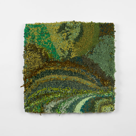 This is a twenty-three-inch square, punch-rug textile made by hand using a variety of textured yarn in various shades of green, ranging from dark olive and forest to light sea foam and teal. The different shades form patches and stripes, the highly textured work is mounted on stretcher bars and hung on the wall.
