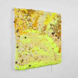 This is a twenty-three-inch square, punch-rug textile made by hand using a variety of textured yarn in different shades of yellow, ranging from bright neon hues to deeper golden shades. The highly textured work is interwoven with white and gold buttons as well as handmade, square ceramic charms that are carved with designs, such as little suns or the phrase “I love Tierra del Sol.” It is mounted on stretcher bars and hung on the wall.