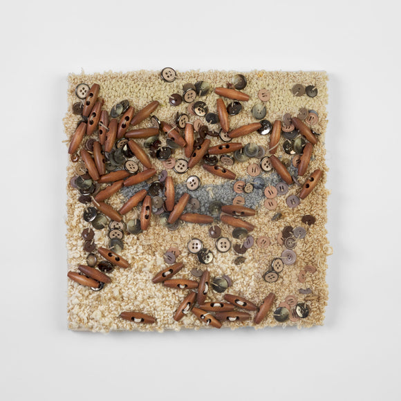 This is a sixteen-inch square, punch-rug textile made by hand using tan, beige, and grey cotton yarn. The surface of the highly textured work is intuitively adorned with dozens of smooth, beige buttons and oblong, wooden beads affixed with tan thread. It is mounted on stretcher bars and hung on the wall.