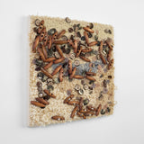 This is a sixteen-inch square, punch-rug textile made by hand using tan, beige, and grey cotton yarn. The surface of the highly textured work is intuitively adorned with dozens of smooth, beige buttons and oblong, wooden beads affixed with tan thread. It is mounted on stretcher bars and hung on the wall.