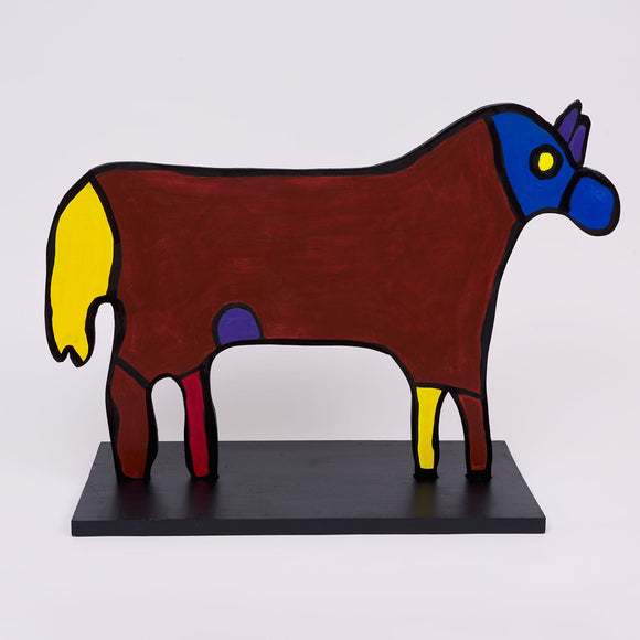 This 19 by 27 by ½-inch wood sculpture by Hugo Rocha features a stylized animal resembling a horse. The body is primarily painted dark sienna with a blue head and a yellow tail. Its eye is yellow, and there are additional yellow and red accents on the legs, with a small purple spot near the belly. The entire figure is outlined in black, adding definition to the simple, bold shapes. The sculpture stands on a black rectangular base, which supports its flat, two-dimensional form.