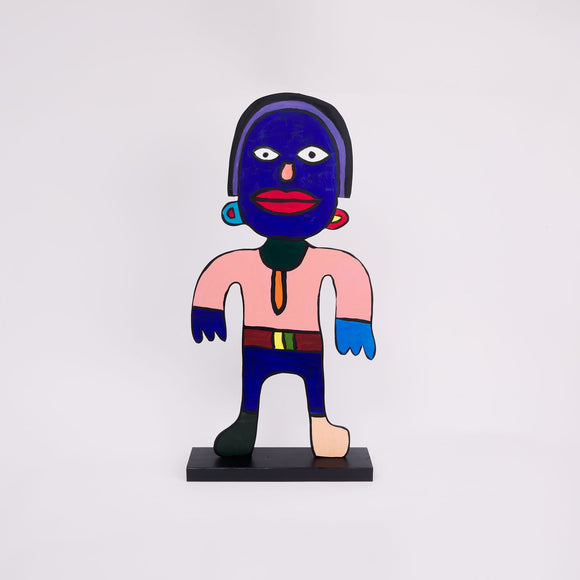 This 37 by 18 by ½-inch wood sculpture by Hugo Rocha portrays a stylized human figure standing upright on a black base. The figure's face is painted blue with wide white eyes and a large red mouth. The body is mostly pink with one hand dark blue and the other light blue. The figure wears a belt with a yellow and green buckle. One foot is dark green, the other beige. The figure has prominent earrings, and a distinct, colorful, abstract appearance, outlined in black for emphasis.