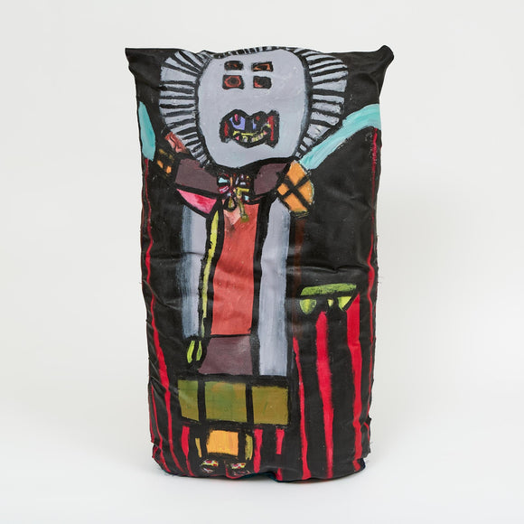 A painted soft sculpture depicting a standing figure with an outlined, mask-like face, big red eyes, and teal and yellow clothing, set against deep green fabric.