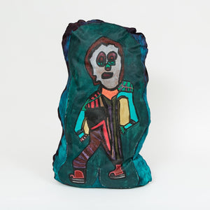 A painted cloth sculpture of a stylized figure with geometric black, pink, and teal patterns, large eyes, and a rectangular torso outlined in yellow and brown.