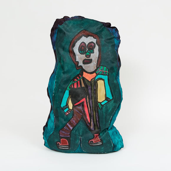 A painted cloth sculpture of a stylized figure with geometric black, pink, and teal patterns, large eyes, and a rectangular torso outlined in yellow and brown.