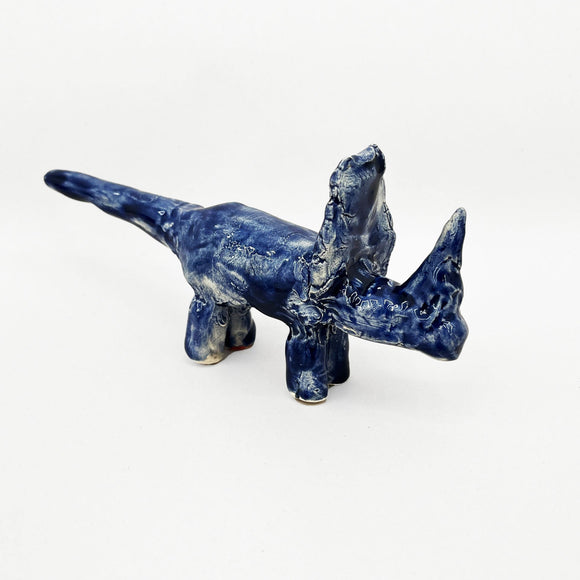 This ceramic sculpture represents a stylized Sinoceratops with a long, elongated snout and pointed horn-like features, finished in a glossy deep blue glaze. The simplified structure and uneven texture give the piece an abstract, primitive quality, blending animalistic elements with a sense of mystery and artistic spontaneity.