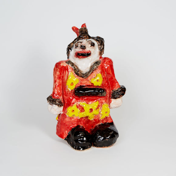 This ceramic Geisha figure, dressed in a vibrant red outfit adorned with yellow floral motifs, captures a whimsical character with an expressive face, highlighted by exaggerated features such as a wide smile and accentuated eyes. The glossy finish and bold colors lend a lively energy to the piece, evoking a sense of playfulness and theatricality.