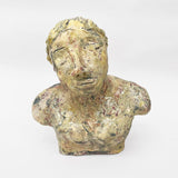 This ceramic bust portrays a figure with a contemplative and somewhat melancholic expression, rendered in a textured, earth-toned glaze that gives the surface a raw, organic quality. The detailing of the face, with its closed or averted eyes and tilted head, suggests a state of introspection or vulnerability, inviting viewers to ponder the emotional depth conveyed by the artist.
