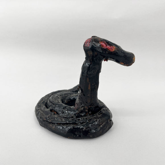 This ceramic sculpture portrays a coiled snake with a raised head, its dark, glossy glaze accentuating the sinuous curves and texture of its body. The piece exudes an ominous presence, with subtle red details near the eyes suggesting a sense of latent aggression or alertness, imbuing the snake with a lifelike and intimidating quality.