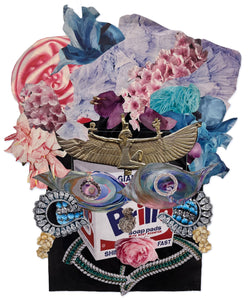 This mixed-media collage combines elements of classical symbolism with pop culture, centering around a Brillo soap pad box framed by an eclectic arrangement of flowers, jewelry, and mythological iconography. The piece juxtaposes the ornate, such as jeweled and floral patterns, with mundane commercial imagery, creating a layered commentary on consumerism, art history, and cultural adornment.