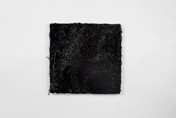 This is a twenty-one-inch square, punch-rug textile made by hand using various shades and textures of black yarn to form a subtle modulation. Loose threads hang from the work’s surface, it is mounted on stretcher bars and hung on the wall.