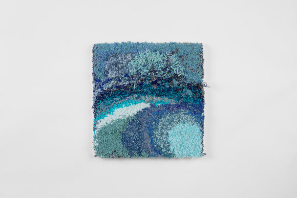 This is an eighteen-inch square, punch-rug textile made by hand using intuitively woven, blue cotton yarn in a range of hues and shades. The highly textured work is mounted on stretcher bars and hung on the wall. 