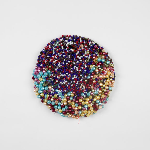 This round, mixed media work consists of densely sewn beads in various sizes and colors including light blue, warm yellow, deep blue, warm pink, and fiery red.