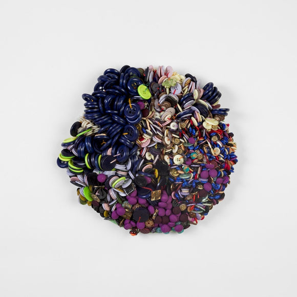 This round, mixed media work consists of hundreds of hand sewn buttons and beads in a variety of colors including deep blues, warm purples, and bright greens.