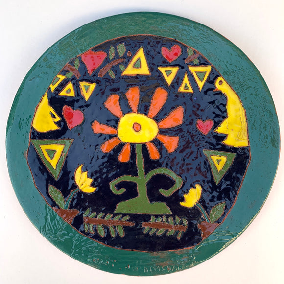 Hand made ceramic tile of a yellow flower with orange petals. Hearts, birds, and branches decorate around the flower. 